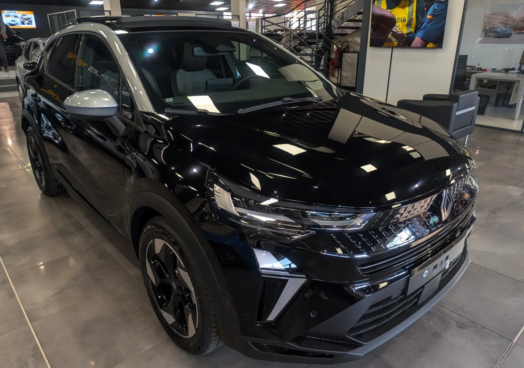 Renault Captur E-Tech hybride 2026 noir avec toit gris, vue 3/4 avant droit en intérieur showroom.
