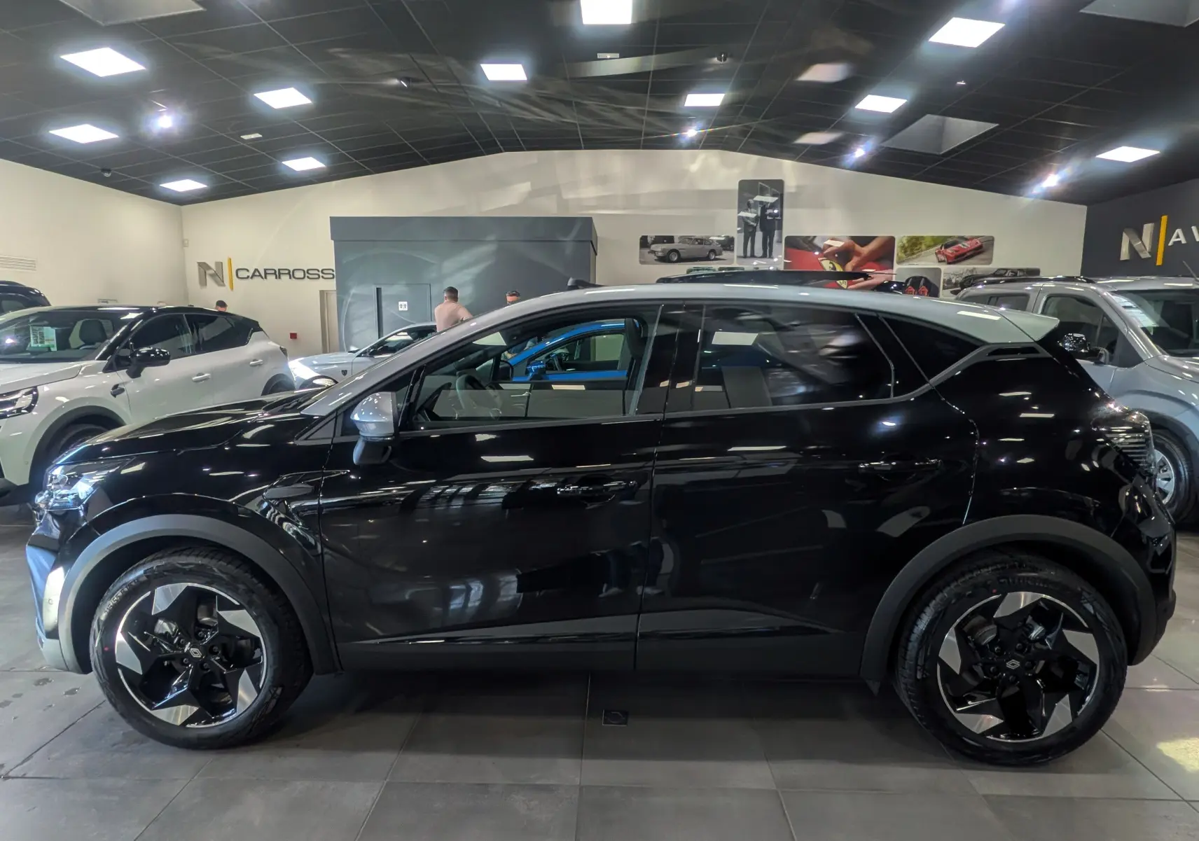 Renault Captur E-TECH 160 CH TECHNO noir avec toit gris Highland, vue profil côté gauche en intérieur showroom.