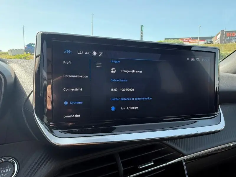 Écran tactile central du tableau de bord du Peugeot 2008 Hybrid 2025, affichant les réglages de langue et de consommation.
