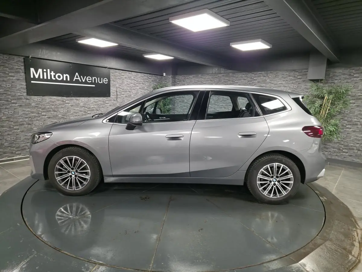 BMW Série 2 218d Active Tourer gris métallisé vue de profil côté gauche en intérieur showroom.