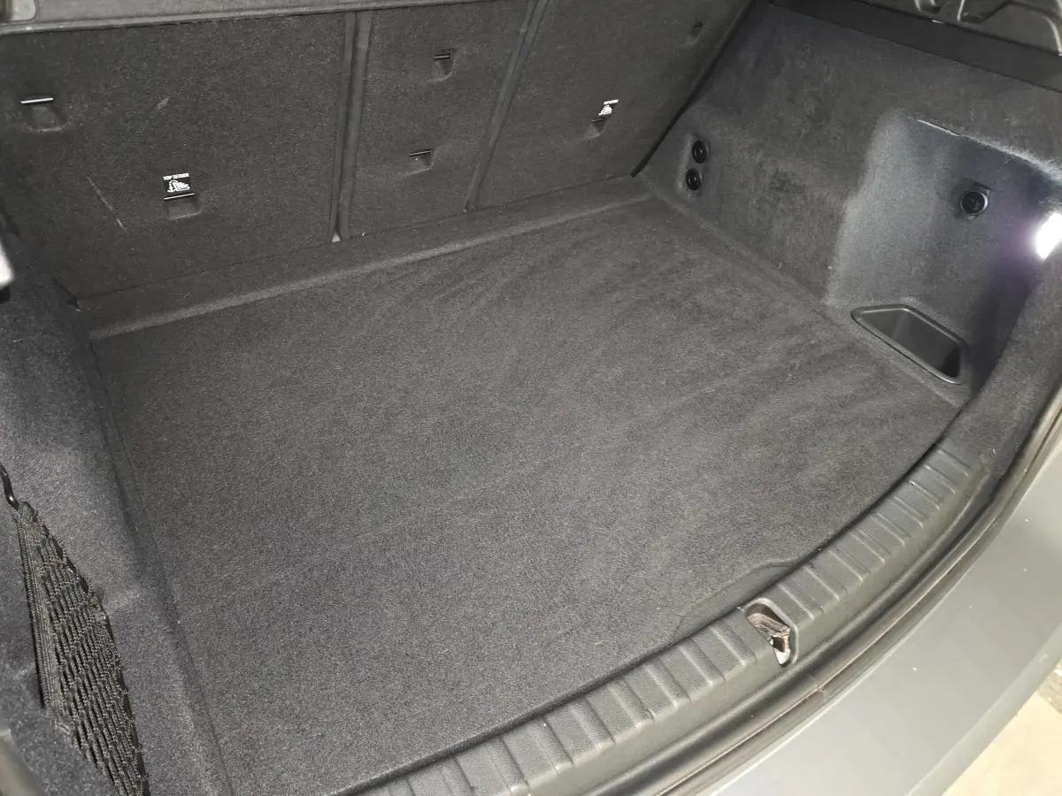 Coffre spacieux de BMW Série 2 218d gris, vue plongeante sur le plancher et les côtés garnis de moquette noire.