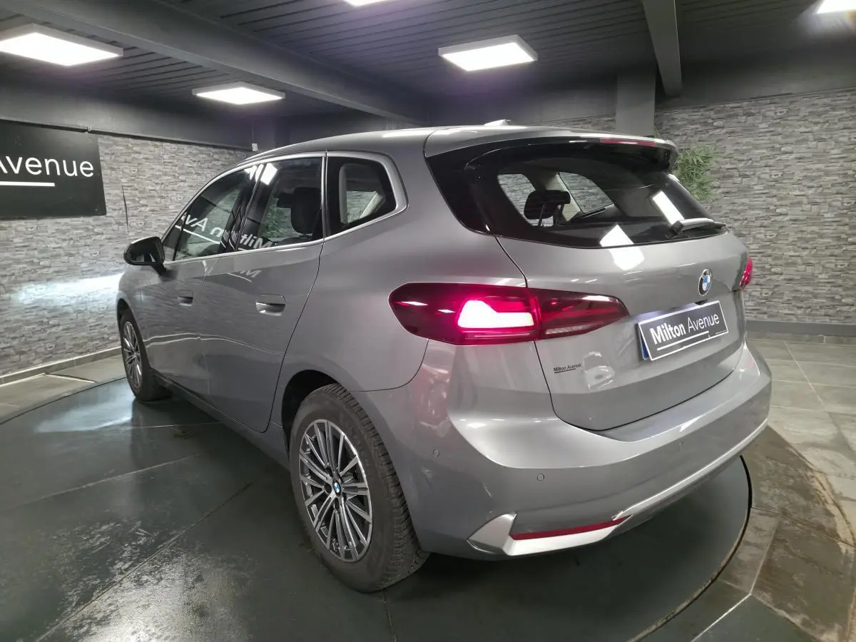 BMW Série 2 218d Active Tourer gris métallisé vue 3/4 arrière avec feux arrière LED allumés en intérieur showroom.