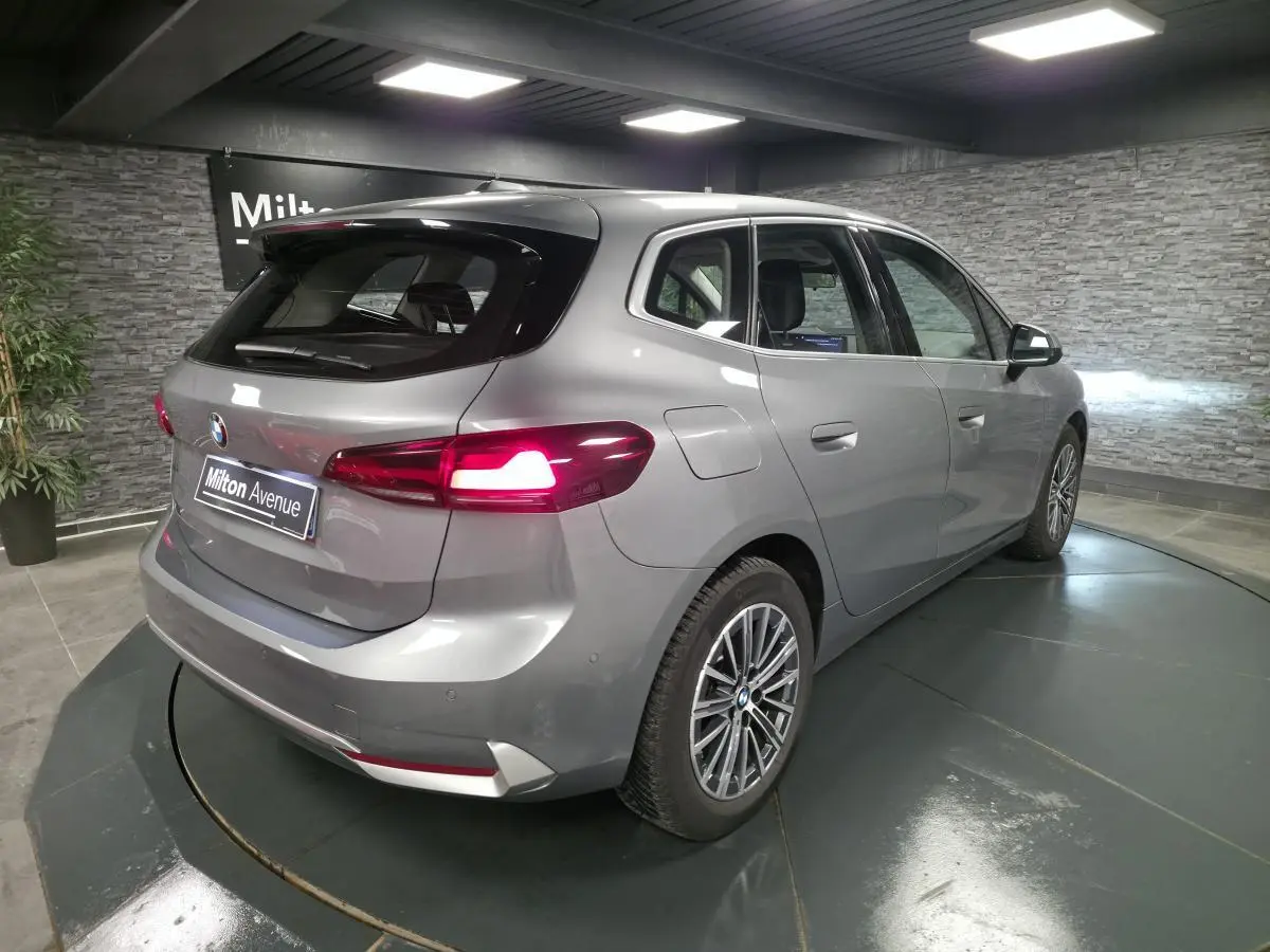 BMW Série 2 218d Active Tourer gris métallisé vue 3/4 arrière droit avec feux arrière allumés et jantes alliage 17 pouces.