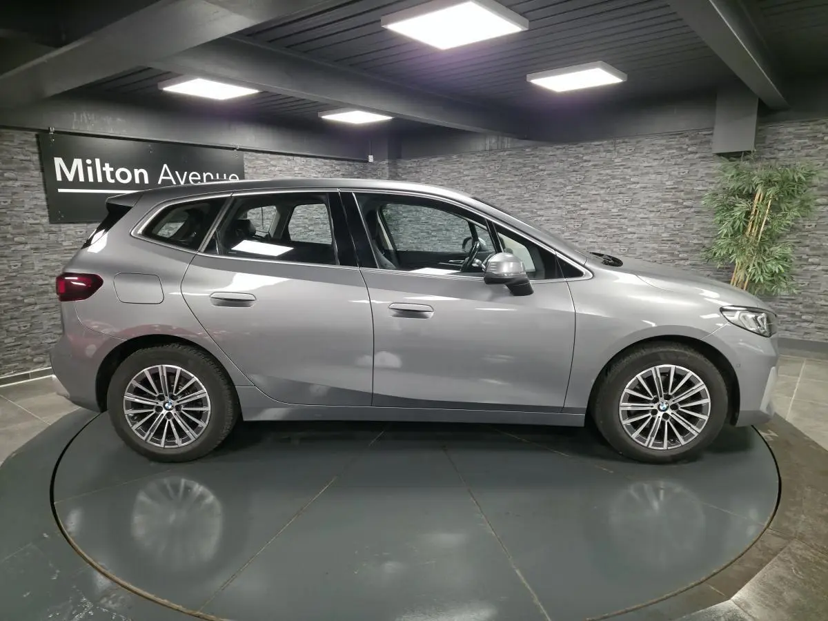BMW Série 2 218d Active Tourer gris métallisé vue de profil côté gauche avec jantes alliage 17 pouces en intérieur showroom.