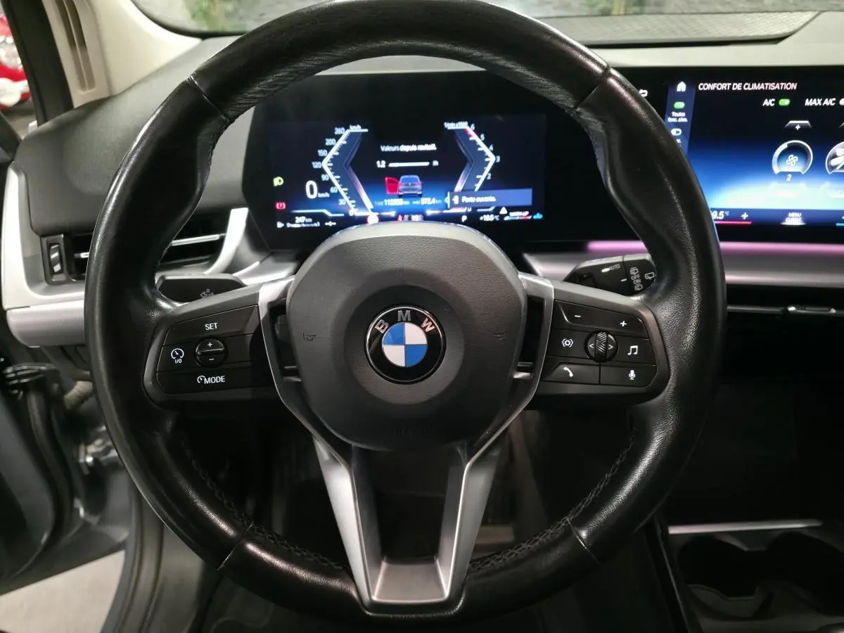 Vue rapprochée du volant cuir noir multifonctions de la BMW Série 2 218d Active Tourer avec tableau de bord numérique.