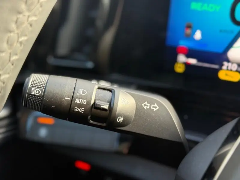 Gros plan sur la commande des feux et clignotants du Renault Austral 2025, intérieur avec écran numérique en arrière-plan.