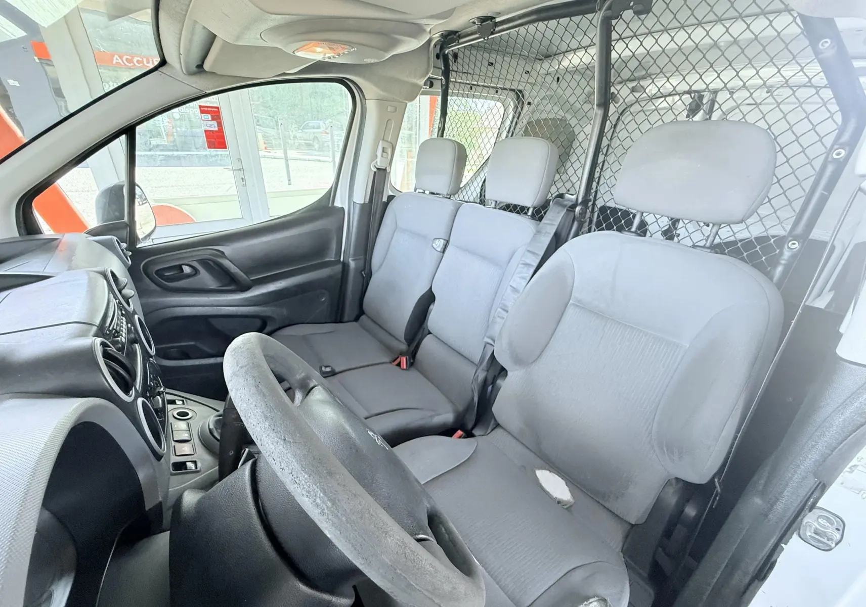 Vue intérieure côté conducteur du Peugeot Partner blanc 2014, montrant les sièges avant et la cloison métallique de séparation.