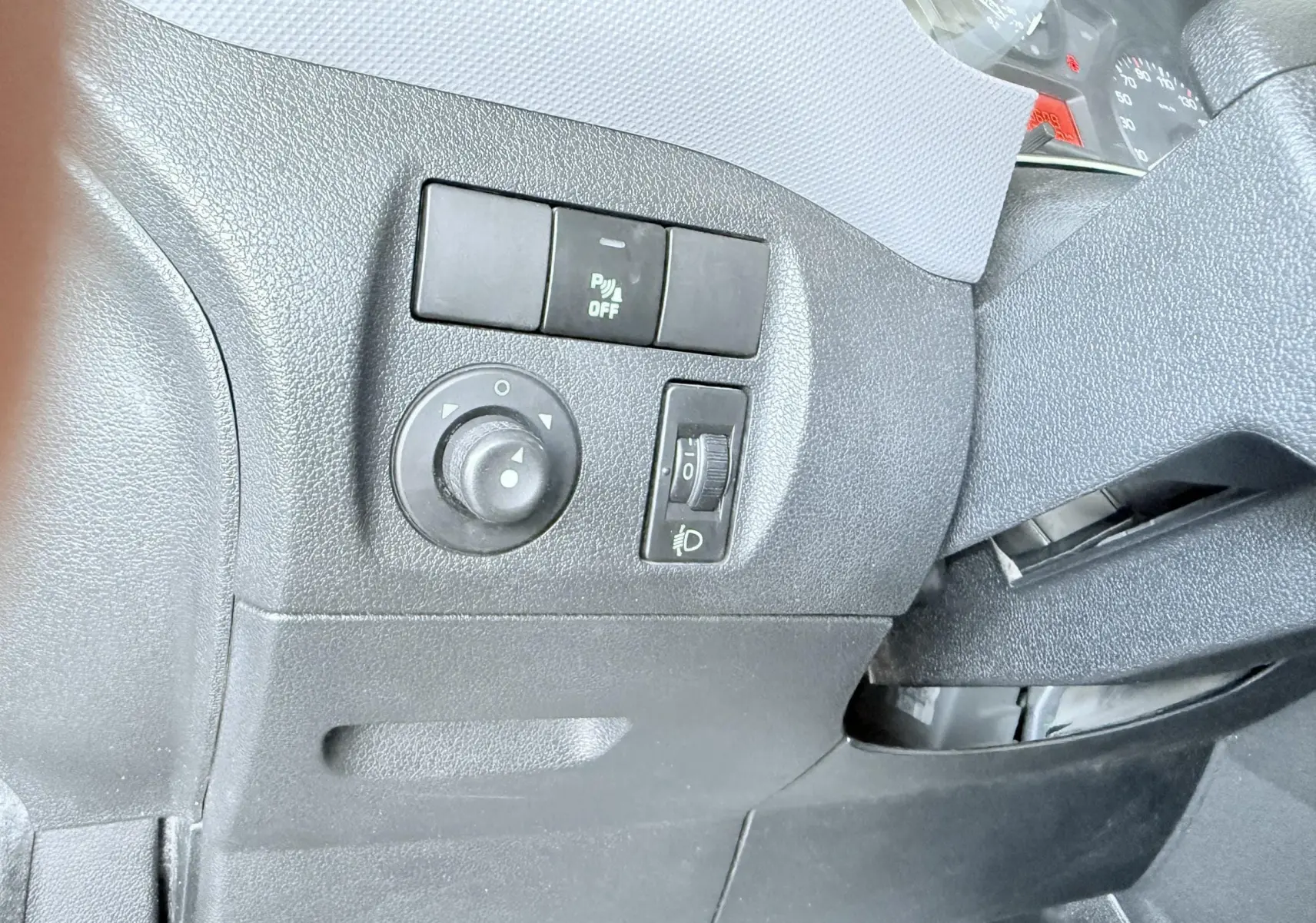 Détail des commandes côté gauche du tableau de bord du Peugeot Partner blanc 2014, avec réglage des rétroviseurs et des phares.