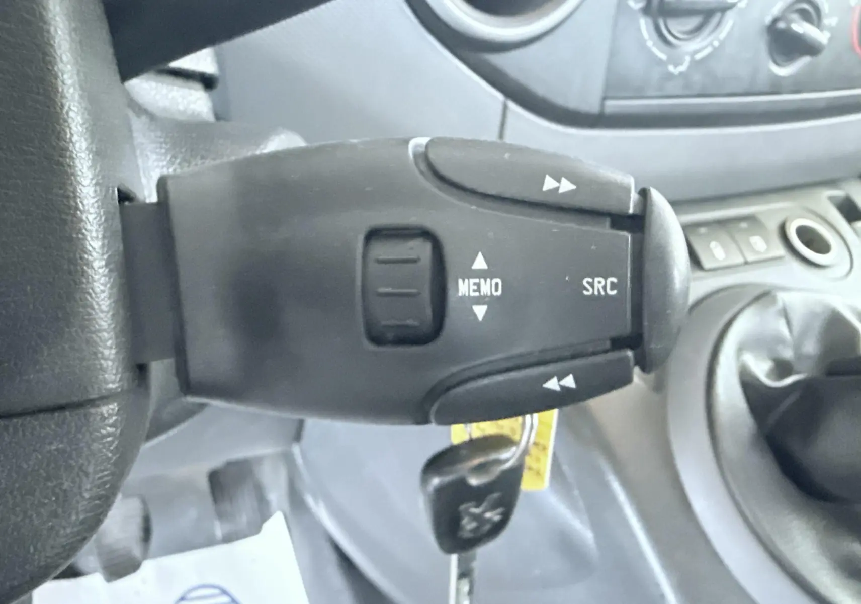 Gros plan sur la commande au volant du Peugeot Partner blanc 2014, avec levier de vitesses manuel visible en arrière-plan.