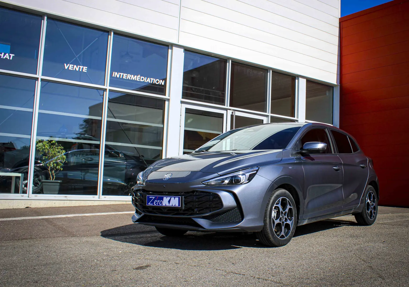 MG3 1.5L Hybrid+ 195ch Luxury en gris Hampstead, vue 3/4 avant droit devant un bâtiment moderne.