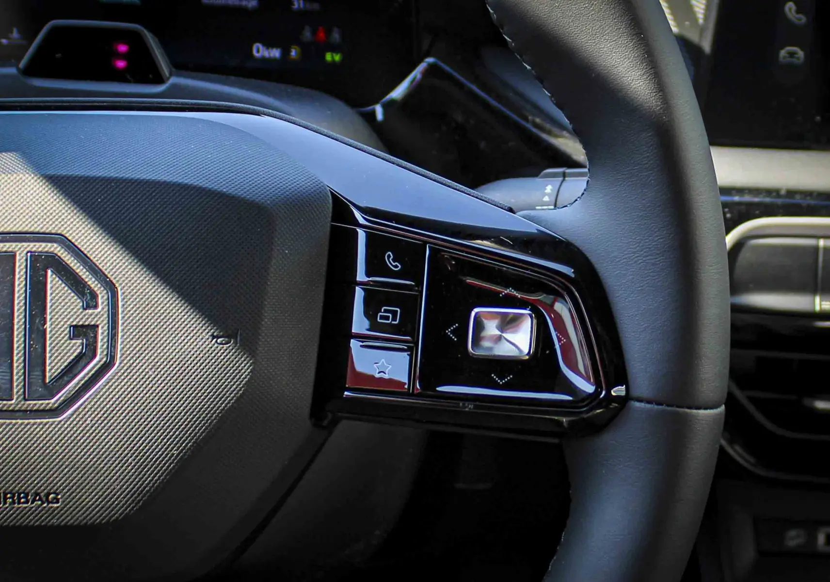 Gros plan sur le volant noir du MG3 1.5L HYBRID+ 195CH Luxury, avec commandes intégrées et logo MG au centre.