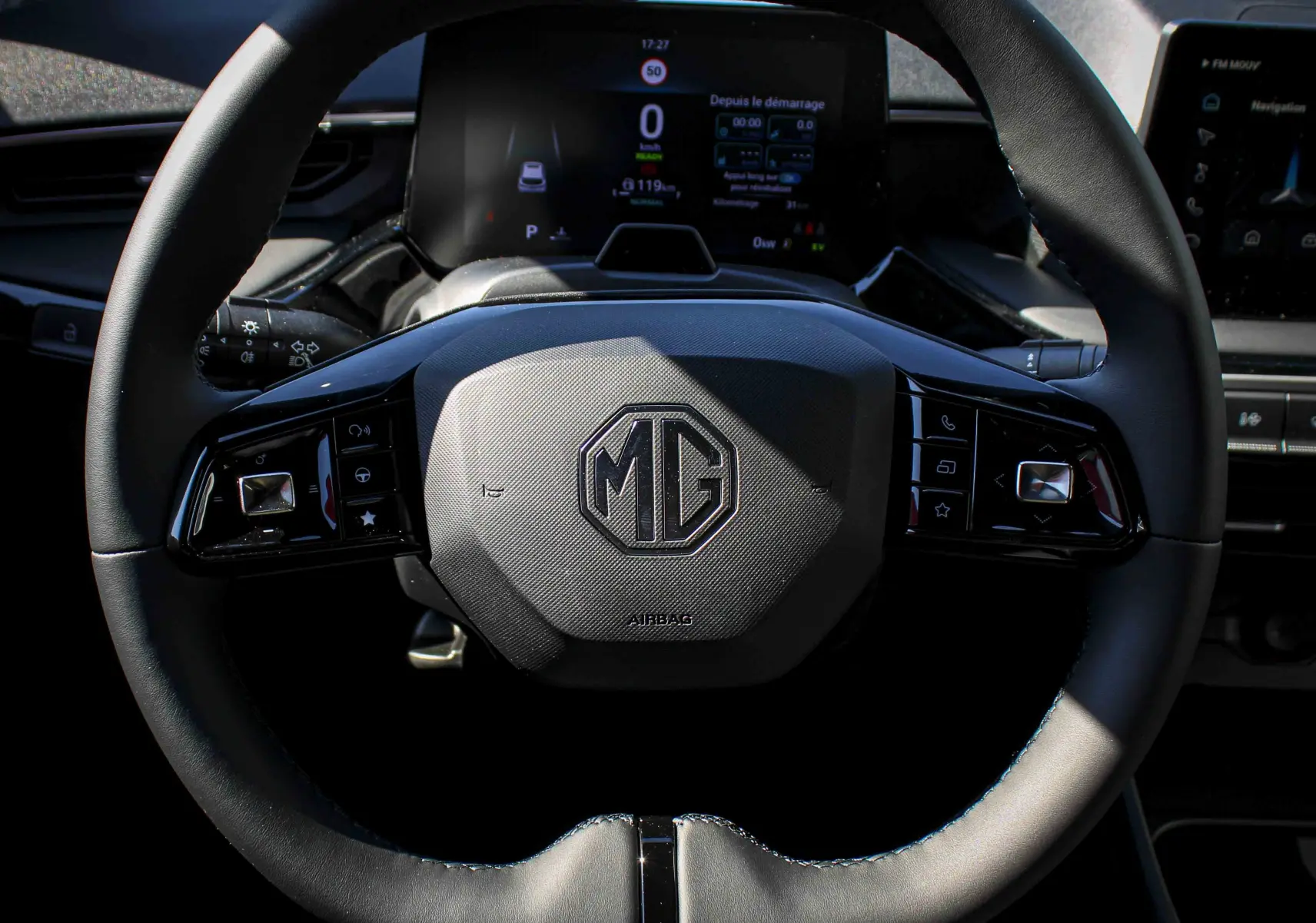 Vue rapprochée du volant noir de la MG3 1.5L HYBRID+ 195CH Luxury avec logo MG centré et tableau de bord digital en arrière-plan.