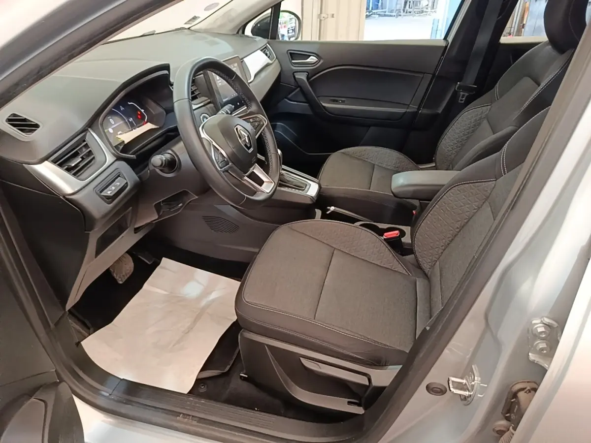 Vue intérieure côté conducteur du Renault Captur gris clair 2022, volant multifonctions en cuir synthétique et sièges tissu gris.