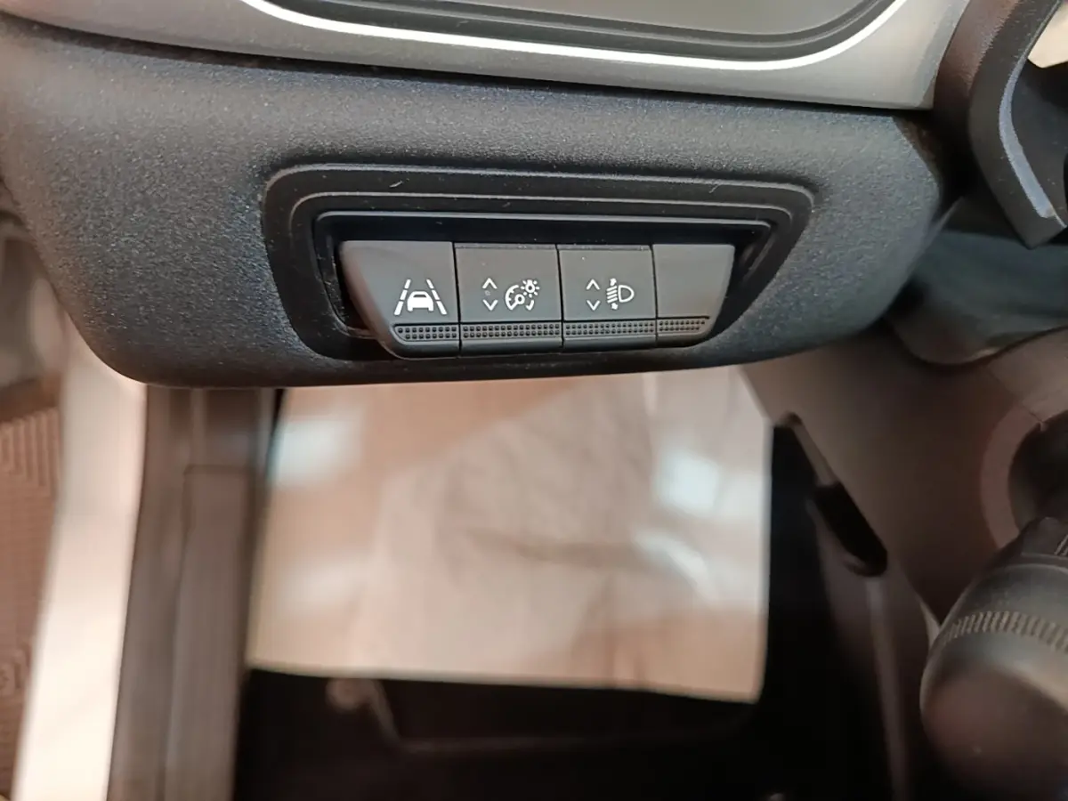 Gros plan sur les boutons de réglage de l'aide au maintien de voie et des phares dans l'habitacle du Renault Captur gris clair.
