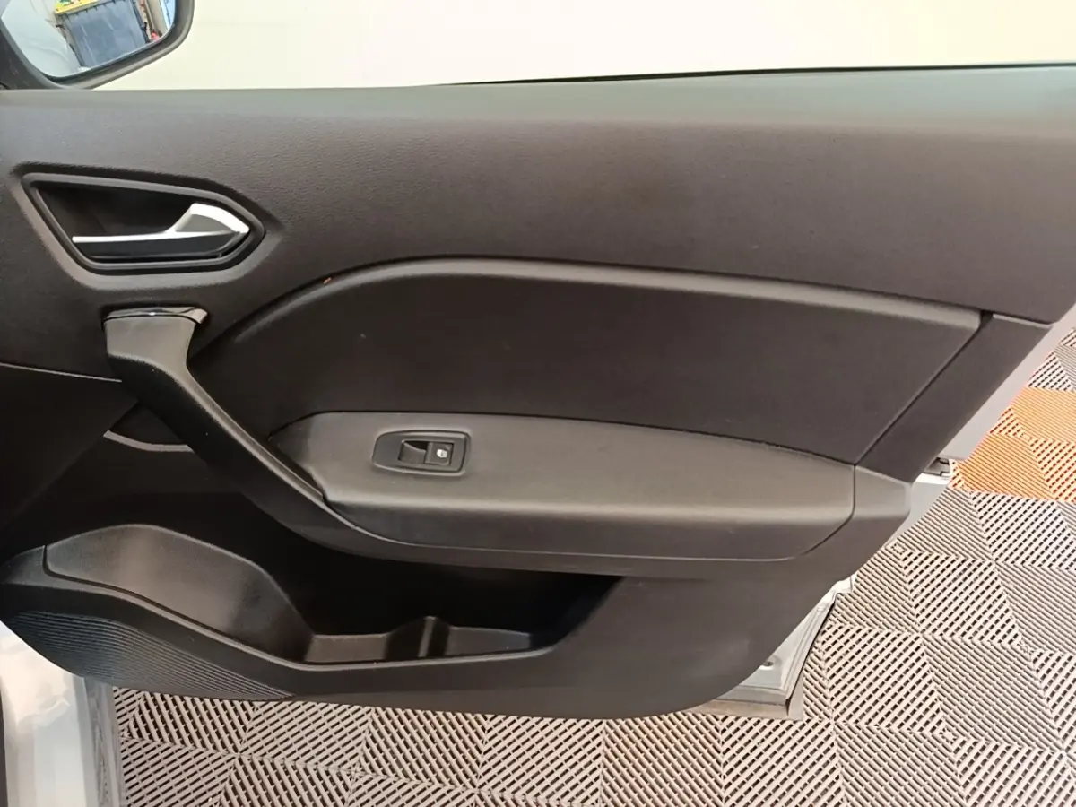 Intérieur côté gauche de la porte avant d’un Renault Captur gris clair, avec poignée et bouton de vitre électrique.