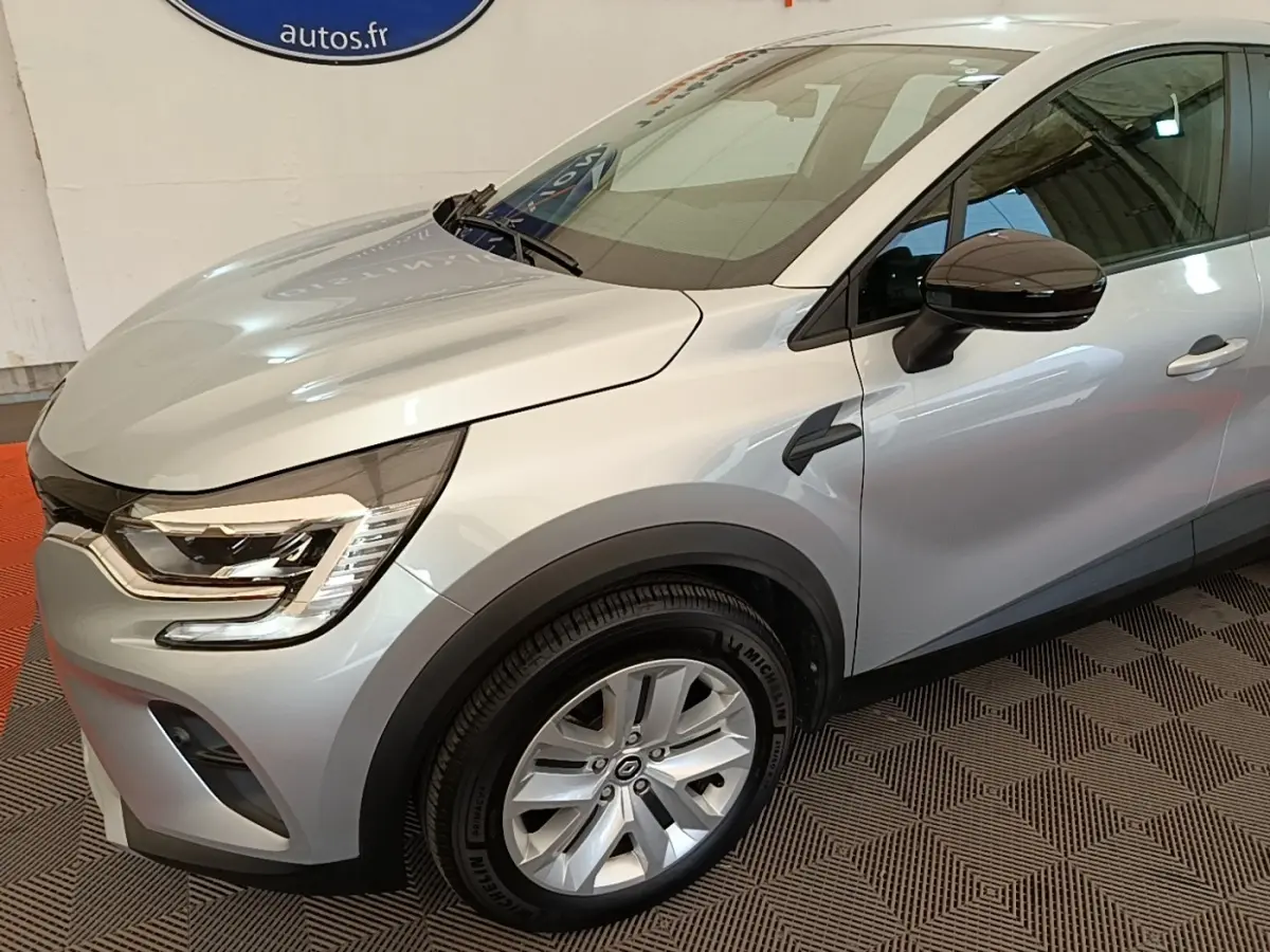Vue 3/4 avant droit du Renault Captur Business E-Tech hybride gris clair avec jantes alliage et rétroviseur noir brillant.