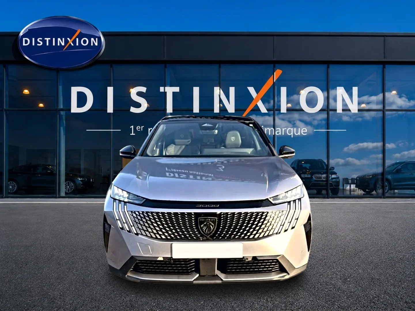 Vue frontale d'un Peugeot 3008 gris 2025 avec calandre distinctive et phares LED fins, devant une vitrine Distinxion.