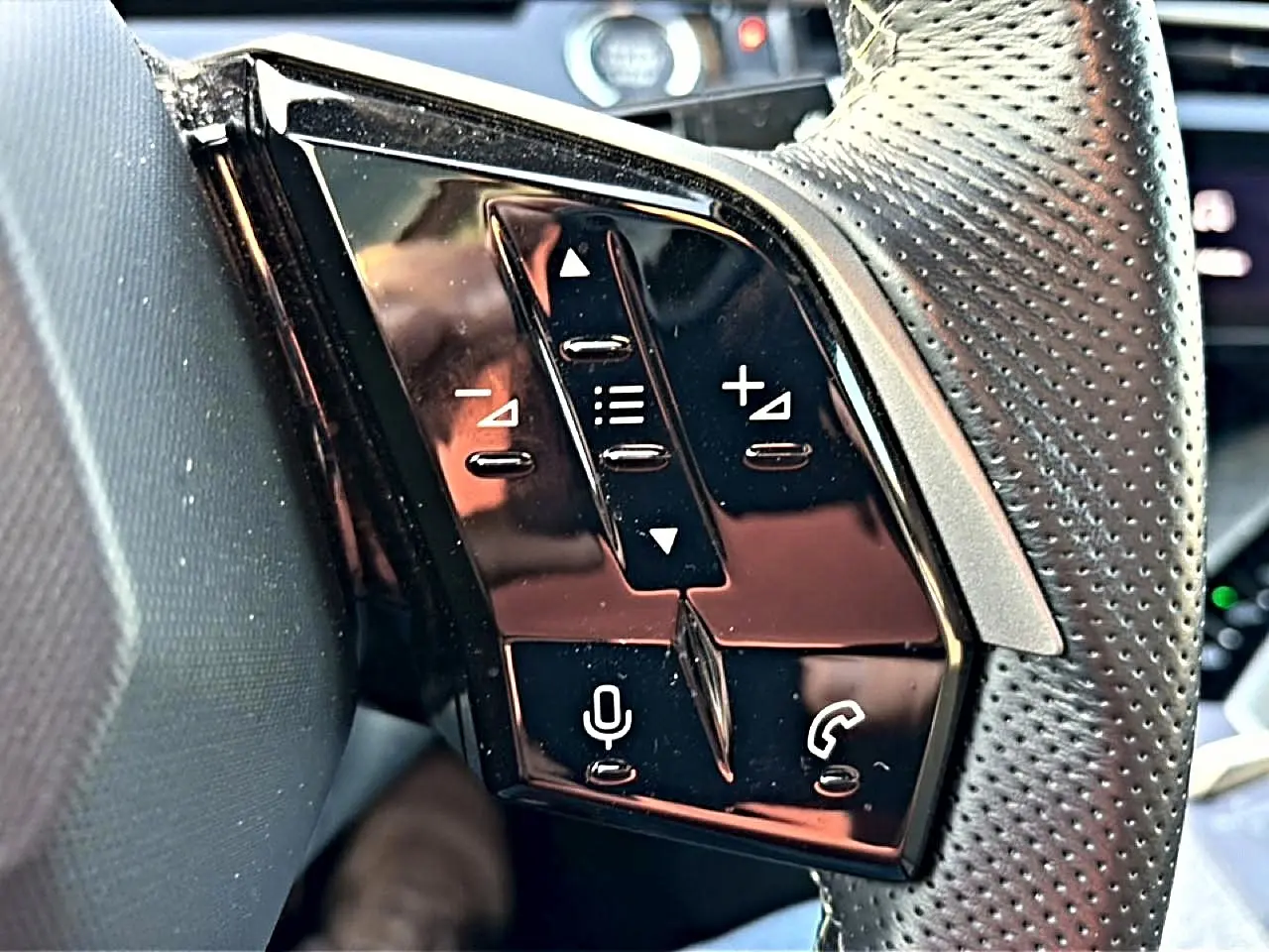 Gros plan sur les commandes vocales et audio noires sur le côté gauche du volant cuir perforé du Peugeot 3008 gris.