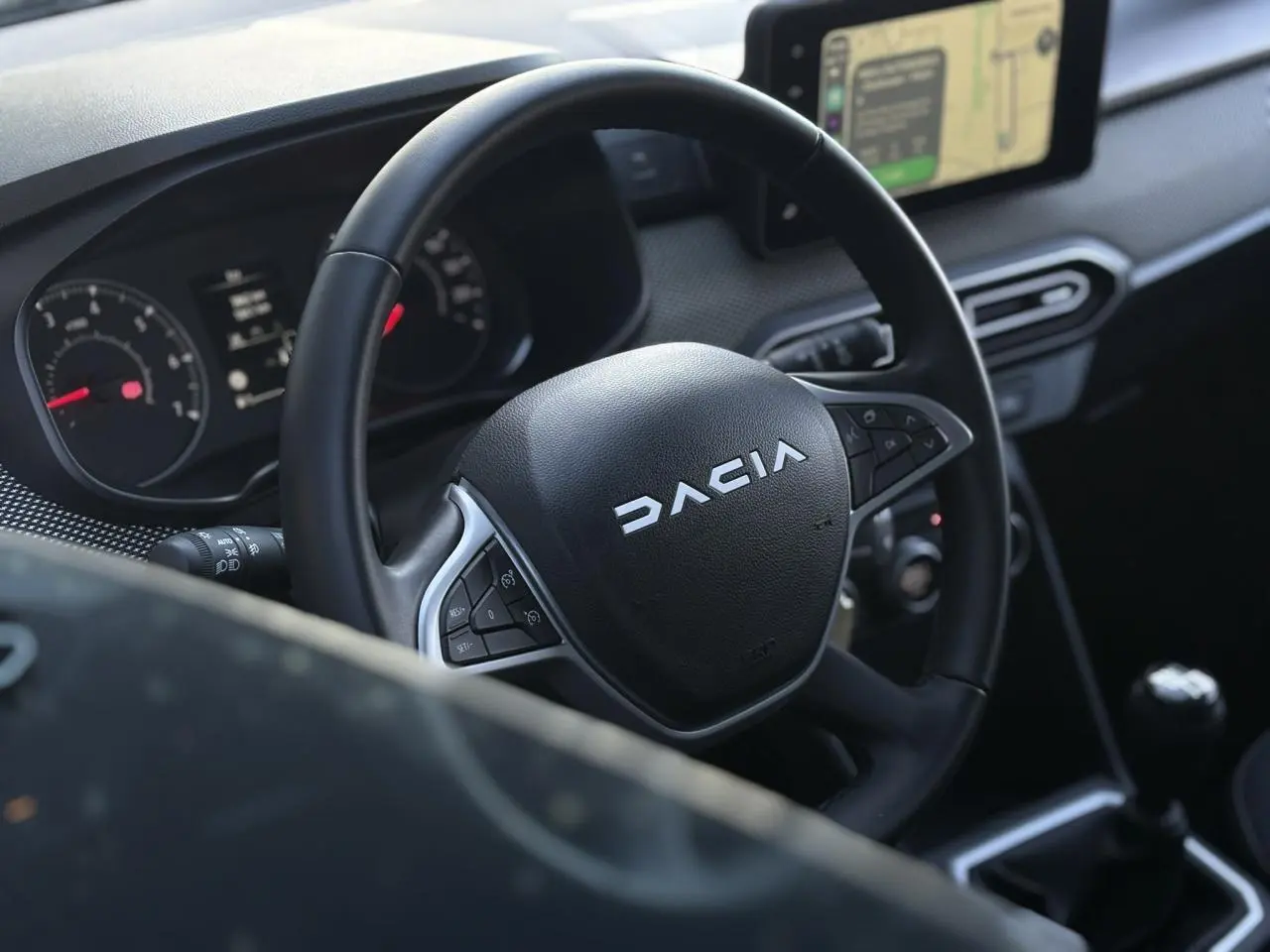 Vue intérieure centrée sur le volant DACIA noir avec tableau de bord et écran tactile GPS en arrière-plan.