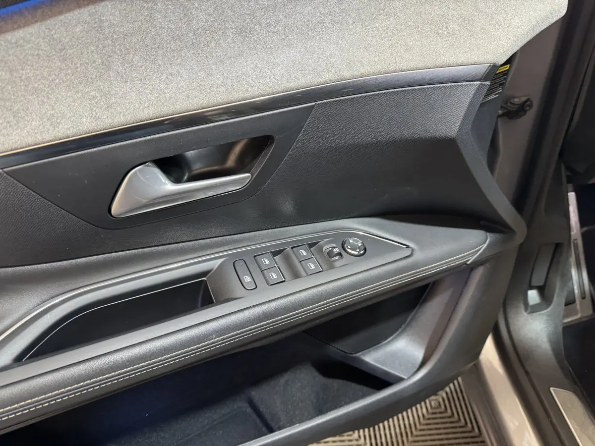 Gros plan sur la porte avant gauche intérieure noire avec commandes des vitres et poignée argentée du Peugeot 3008 gris clair.