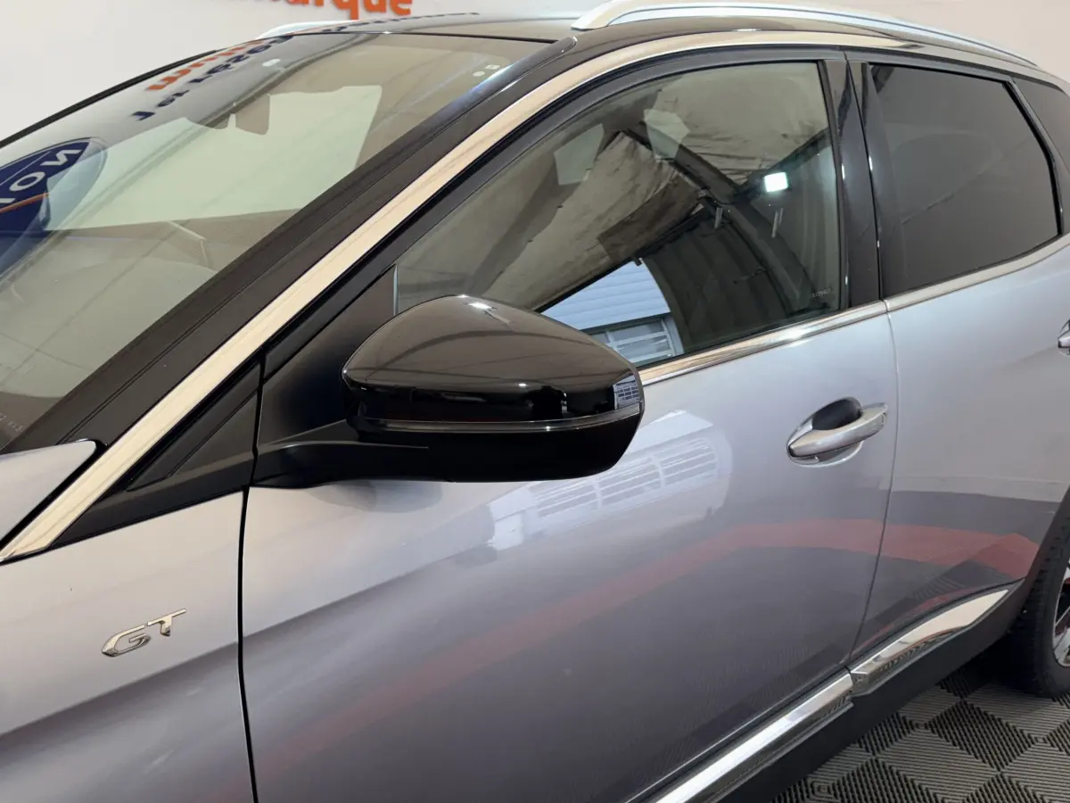 Vue latérale côté gauche d’un Peugeot 3008 GT gris clair avec rétroviseur noir brillant et badge GT visible.