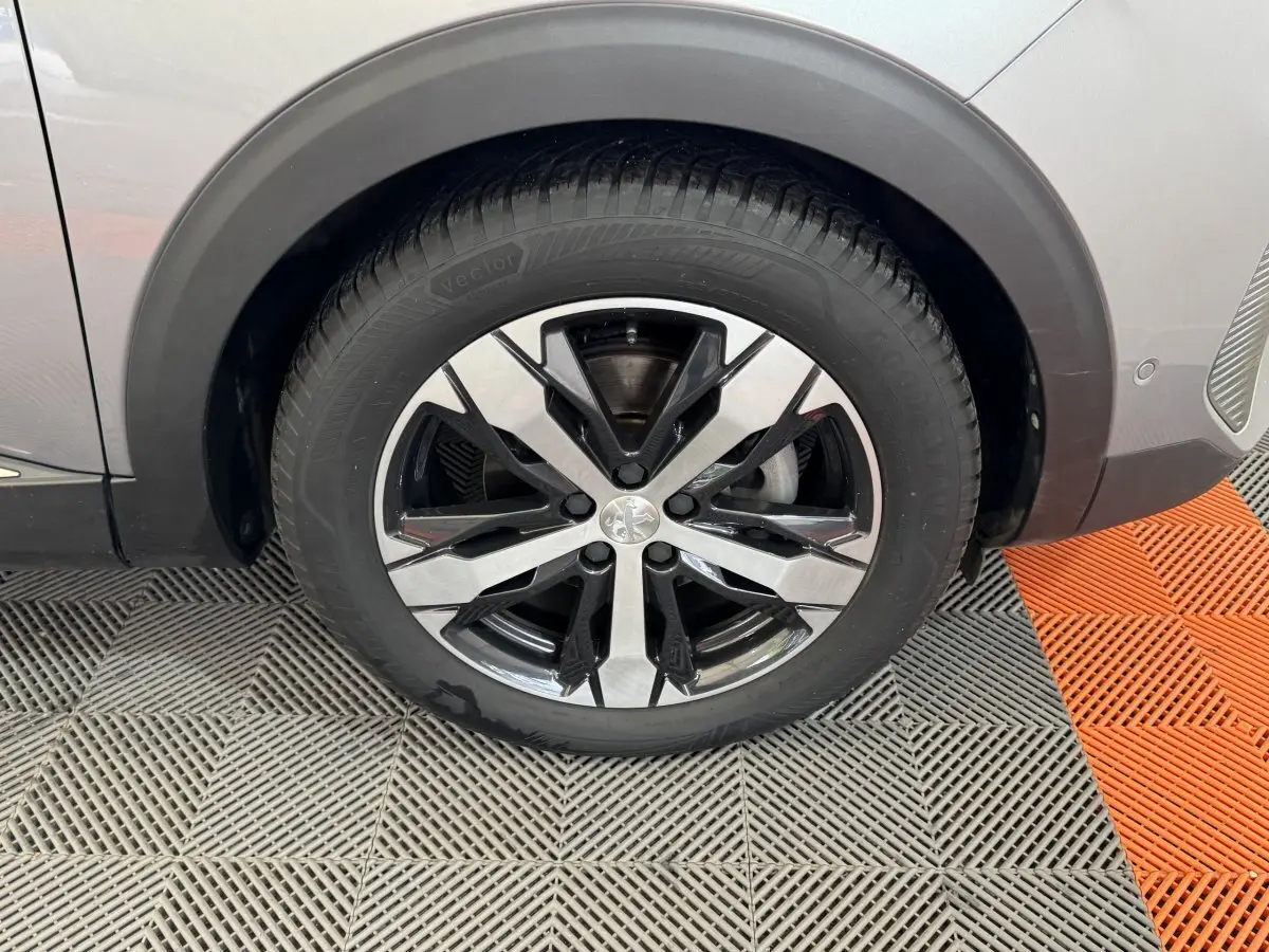 Gros plan sur la roue avant droite du Peugeot 3008 gris clair, mettant en valeur la jante alliage bicolore moderne.
