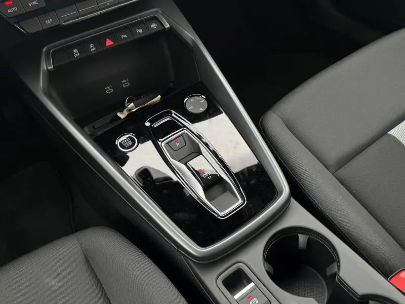 Vue rapprochée de la console centrale noire de l’Audi A3 Sportback 30 TFSI hybride avec levier de vitesse automatique et sièges tissu gris.