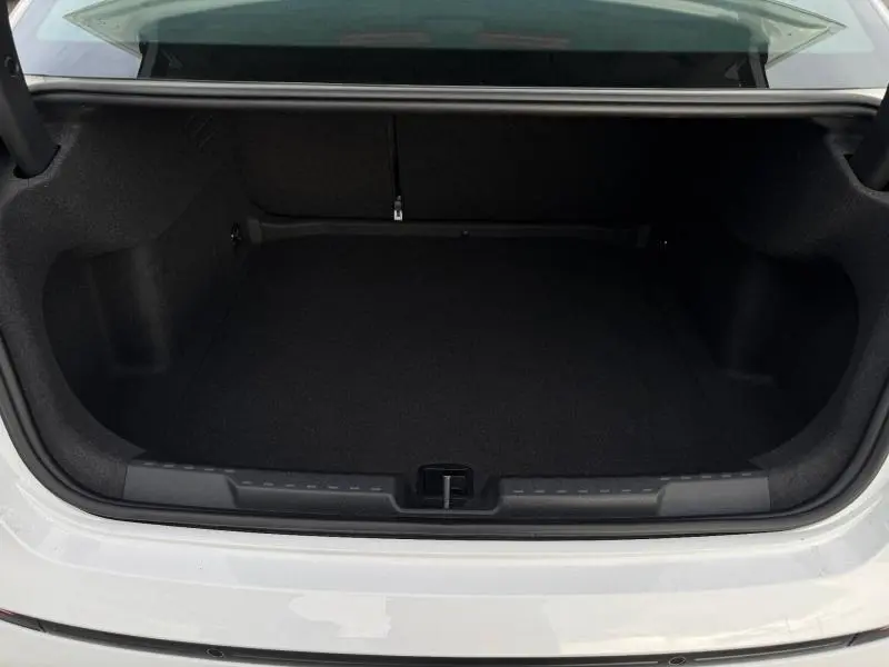 Coffre ouvert vu de l'arrière d'une Audi A3 Sportback blanche 2024, espace de rangement vide et tapis noir.