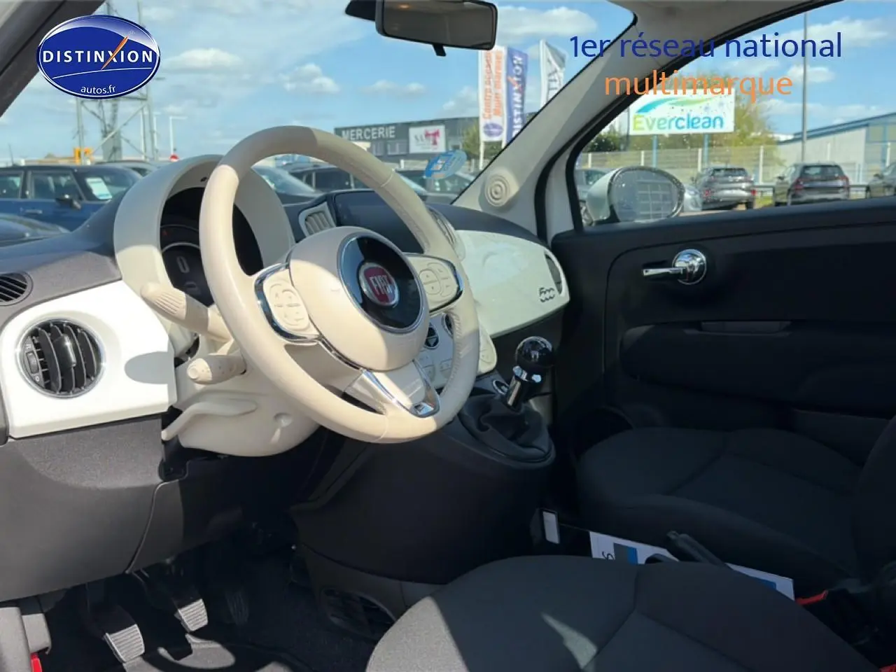 Intérieur avant droit d'une Fiat 500 blanche 2023 avec volant cuir beige et tableau de bord assorti.