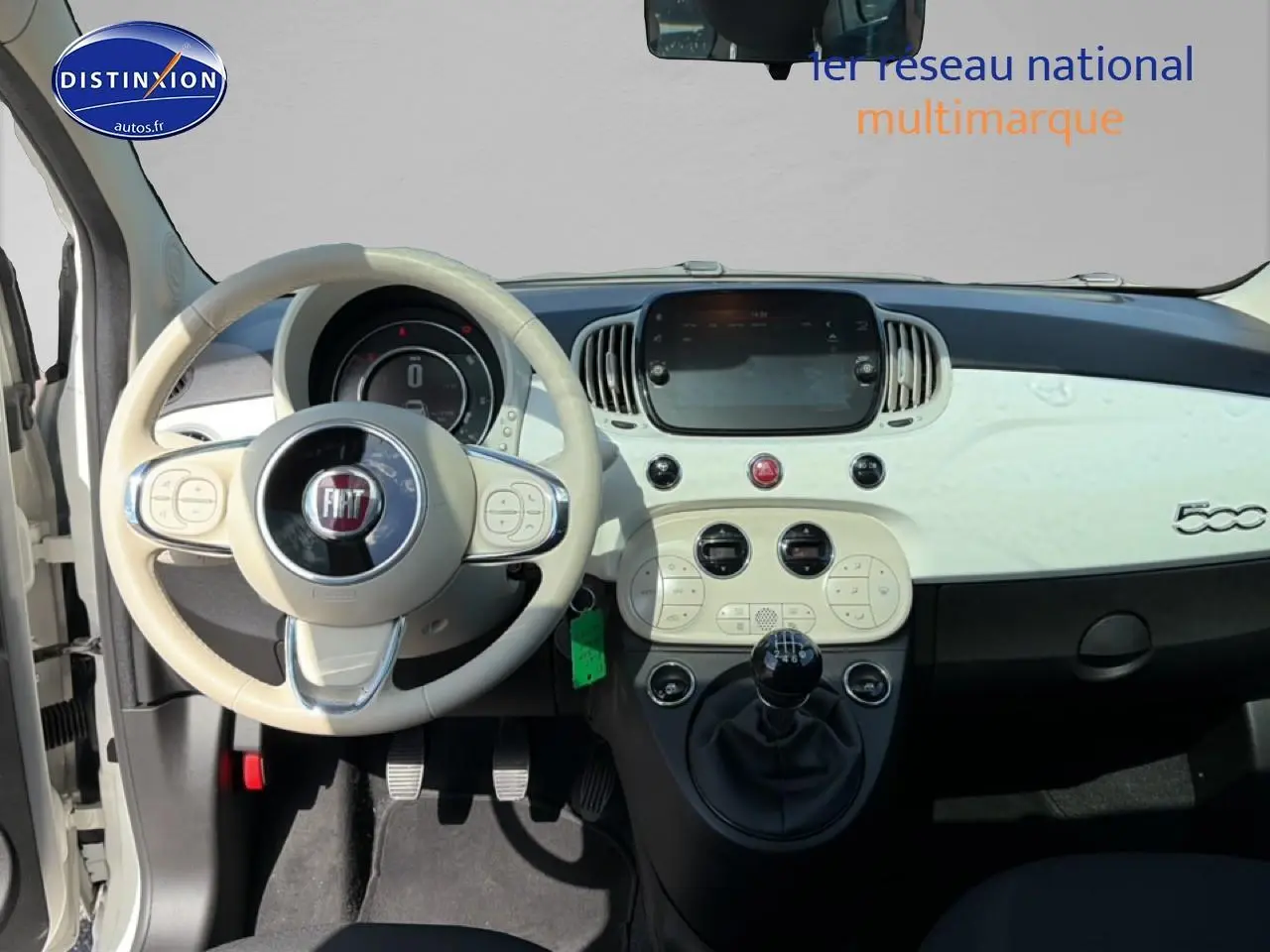 Vue intérieure avant centrée sur le tableau de bord blanc et volant beige de la Fiat 500 2023 avec boîte manuelle.