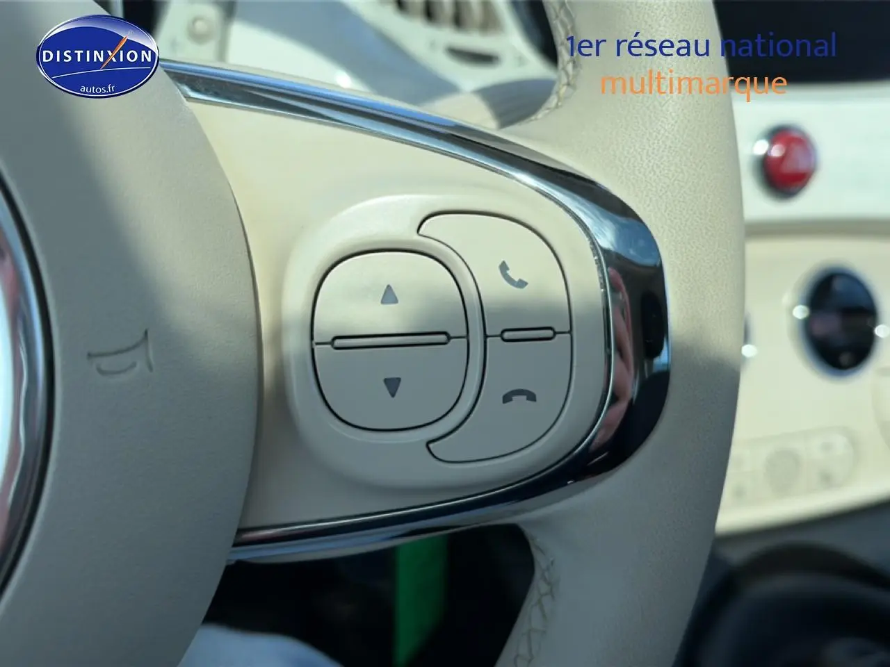 Gros plan sur les commandes du volant beige de la Fiat 500 blanche, avec boutons de gestion d'appels et volume.