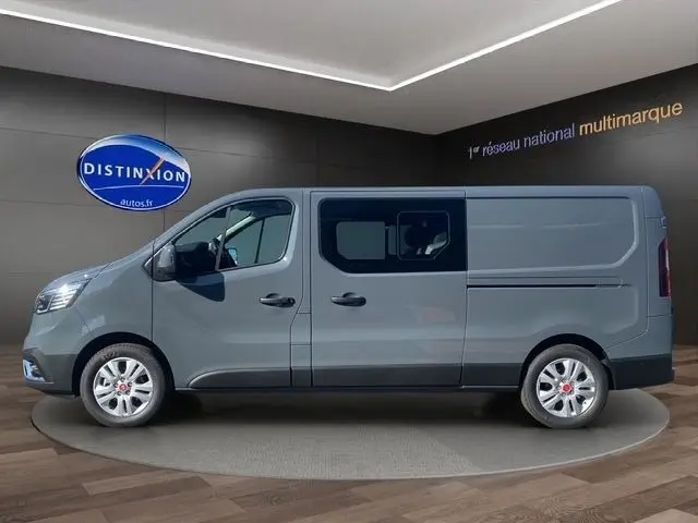 Vue latérale droite d’un Renault Trafic Fourgon gris foncé avec fenêtres sur la cabine, en intérieur showroom.