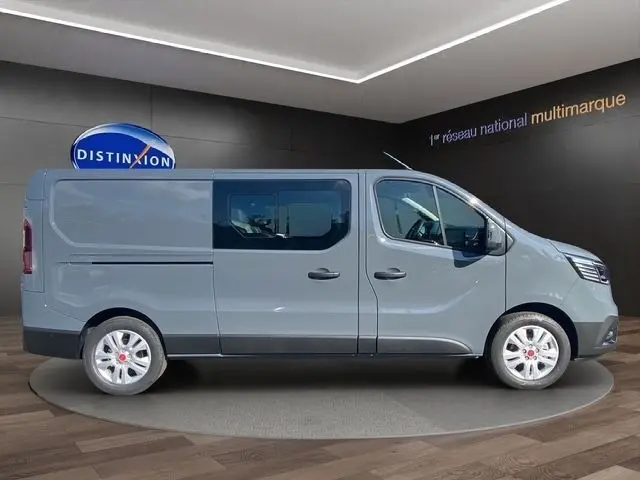 Vue latérale droite d'un Renault Trafic Fourgon gris foncé avec fenêtres latérales et jantes argentées, en intérieur showroom.