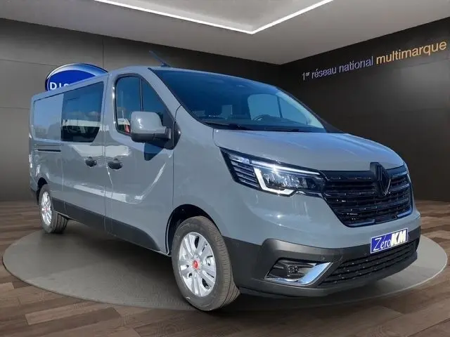 Vue 3/4 avant d'un Renault Trafic Fourgon gris foncé avec calandre noire et phares LED allumés dans un showroom.