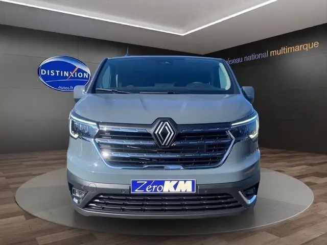 Vue de face du Renault Trafic Fourgon gris foncé avec calandre chromée et feux LED allumés en showroom.