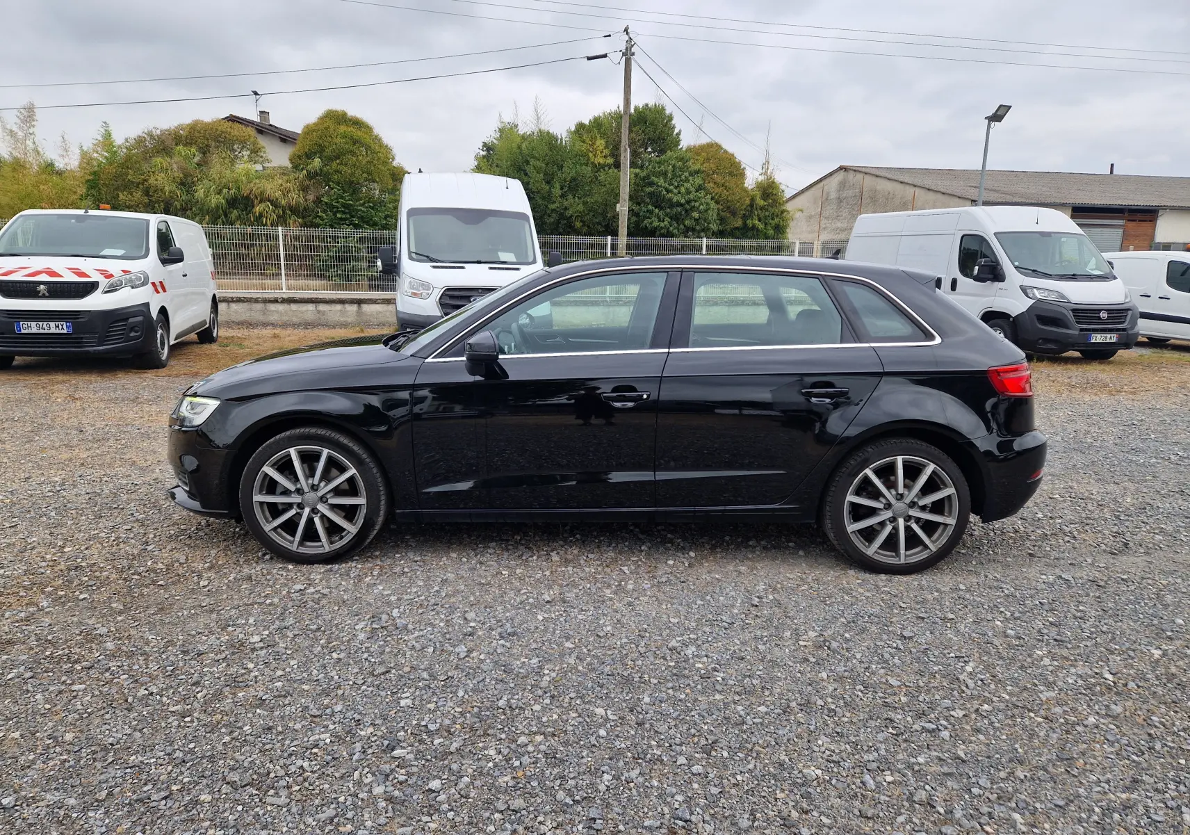 Profil côté gauche d'une Audi A3 Sportback noire 2019, avec jantes alliage 18 pouces sur un sol gravillonné.