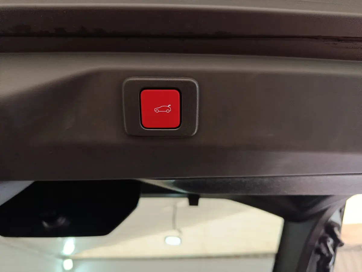 Bouton rouge d'ouverture électrique du coffre sur le hayon intérieur d'un Peugeot 3008 noir hybride 2025.