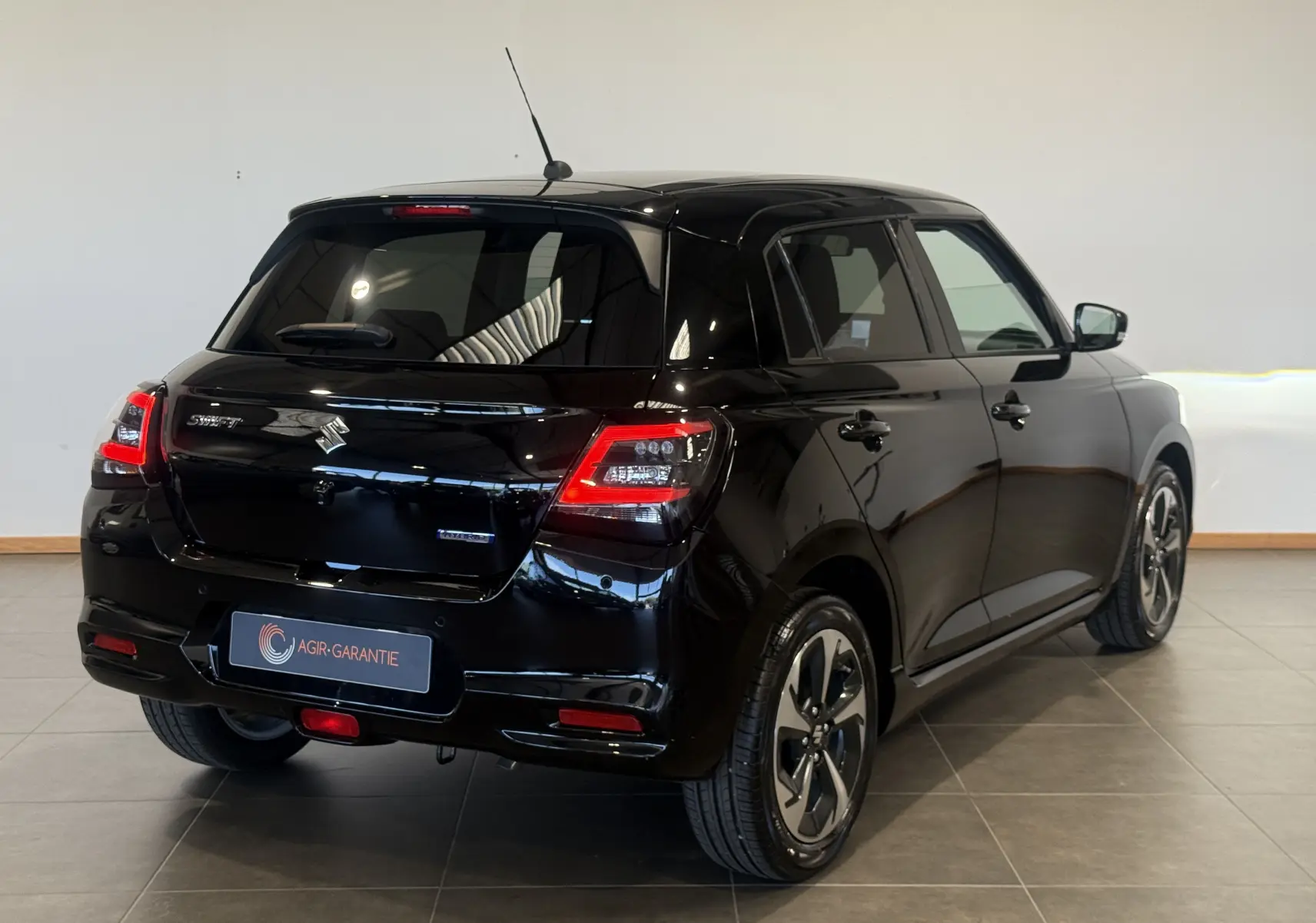 Suzuki Swift 2025 noire vue 3/4 arrière droit, avec feux arrière allumés et jantes alliage distinctives.