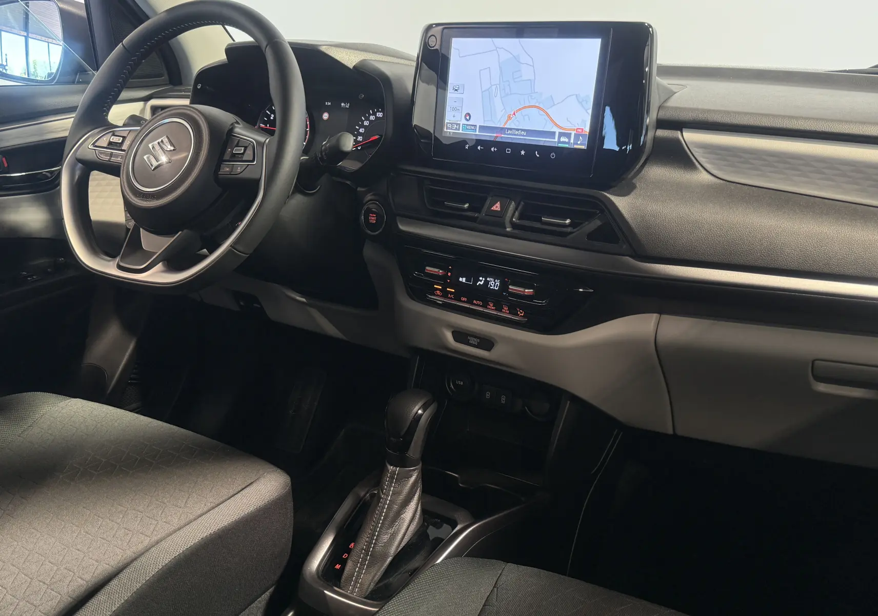 Intérieur avant droit de la Suzuki Swift 2025 noire, avec volant multifonction, écran tactile et boîte automatique.