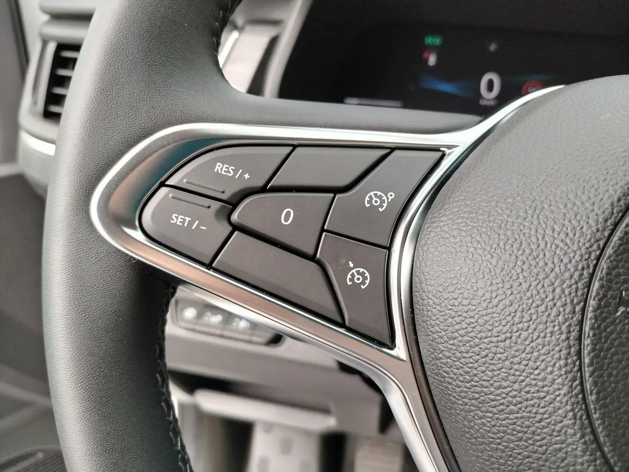 Gros plan sur les commandes de régulateur de vitesse au volant noir du Nissan Primastar blanc 2025.