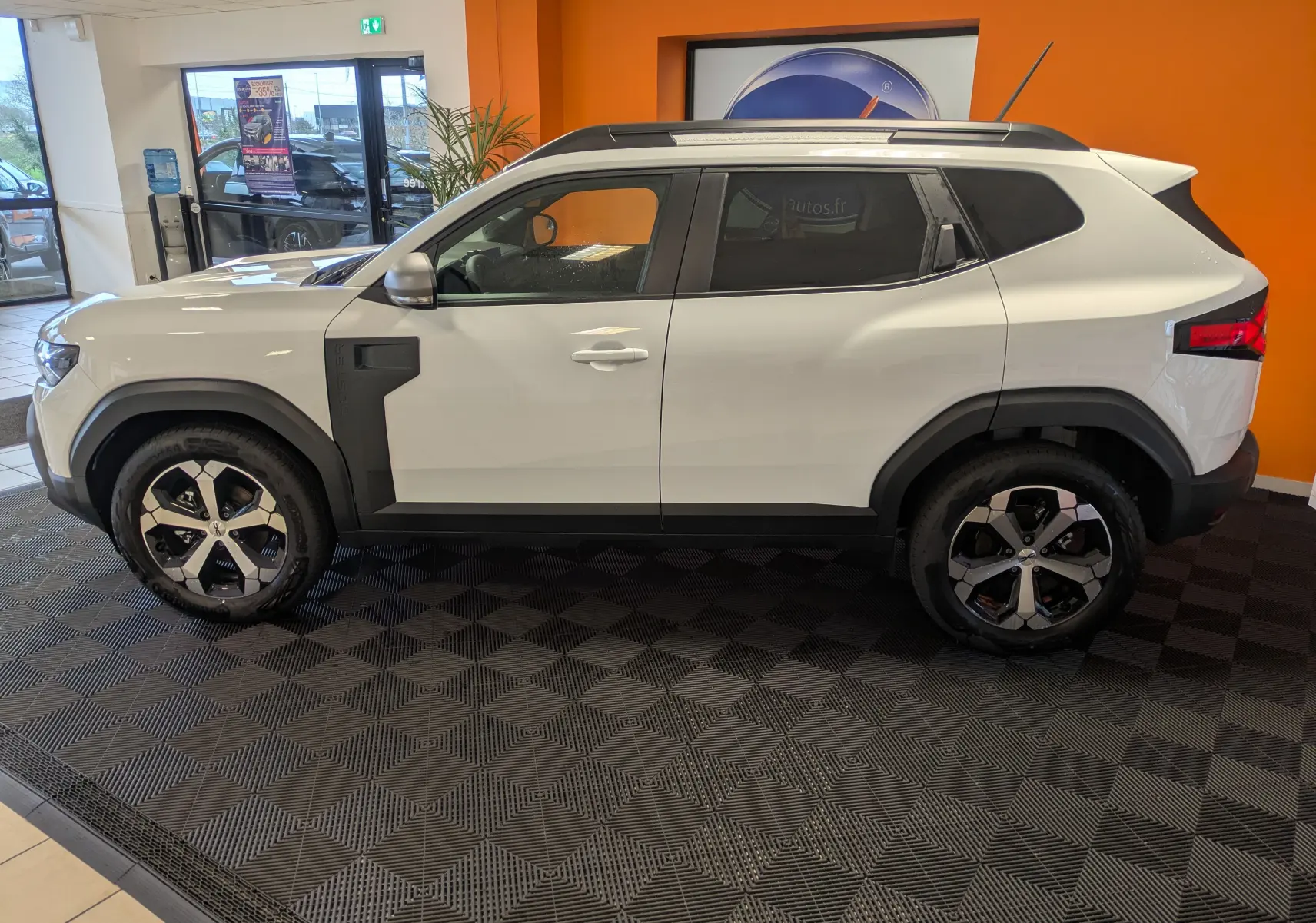 Vue de profil côté gauche d'un Dacia Duster Hybrid 140 Journey blanc glacier avec jantes alliage 18 pouces en intérieur showroom.