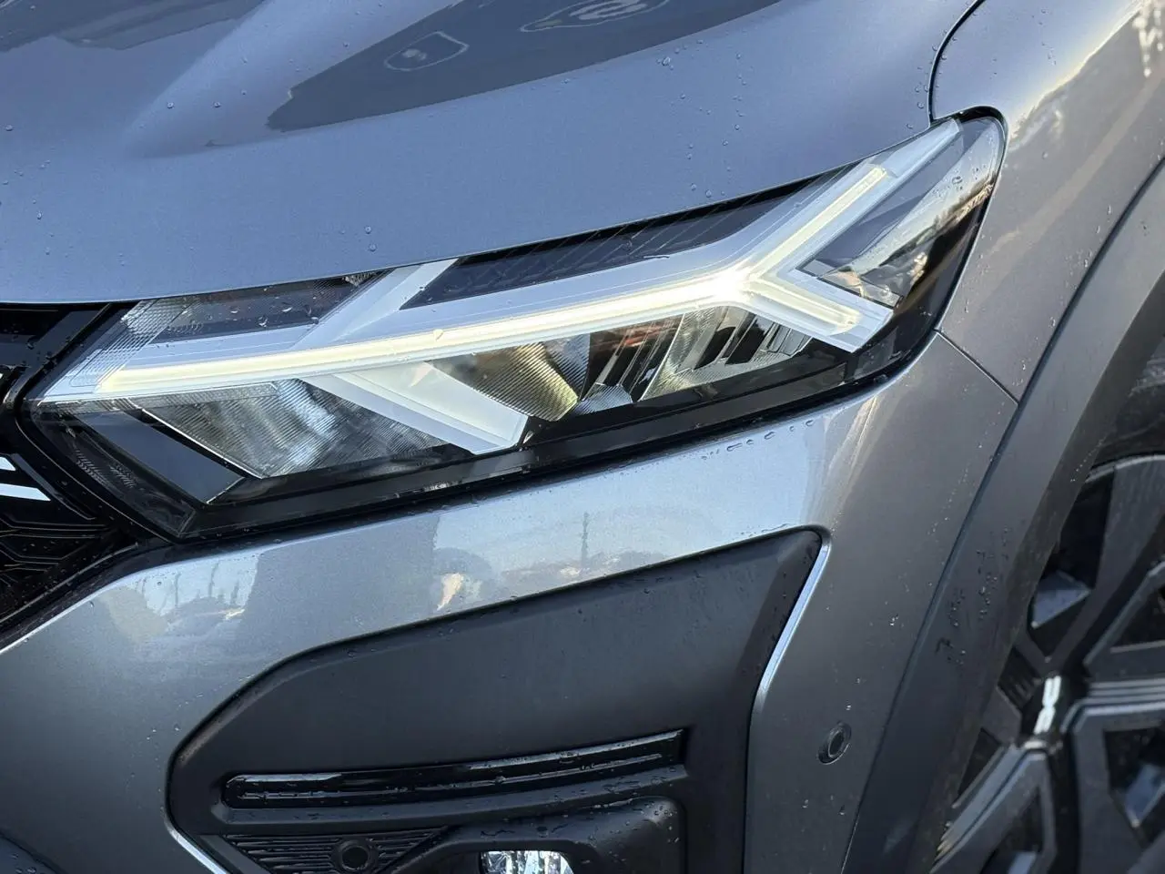 Gros plan sur le phare avant droit du Dacia Jogger gris schiste, mettant en valeur la signature lumineuse LED en forme de flèche.