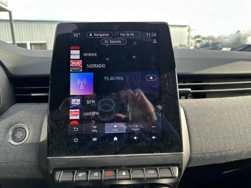 Vue rapprochée de l’écran tactile central de la Renault Clio 2025 avec affichage des radios et bouton Start Engine Stop à gauche.