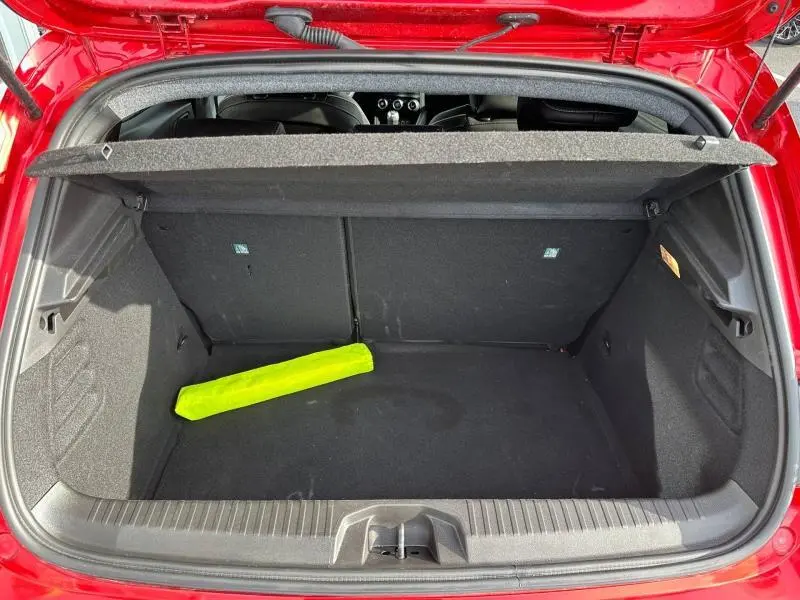 Vue plongeante sur le coffre ouvert d'une Renault Clio 2025 Rouge Flamme avec un triangle de signalisation jaune à l'intérieur.