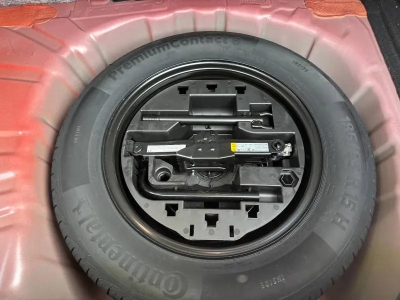 Gros plan sur la roue de secours et les outils de bord dans le coffre rouge flamme d'une Renault Clio 2025.