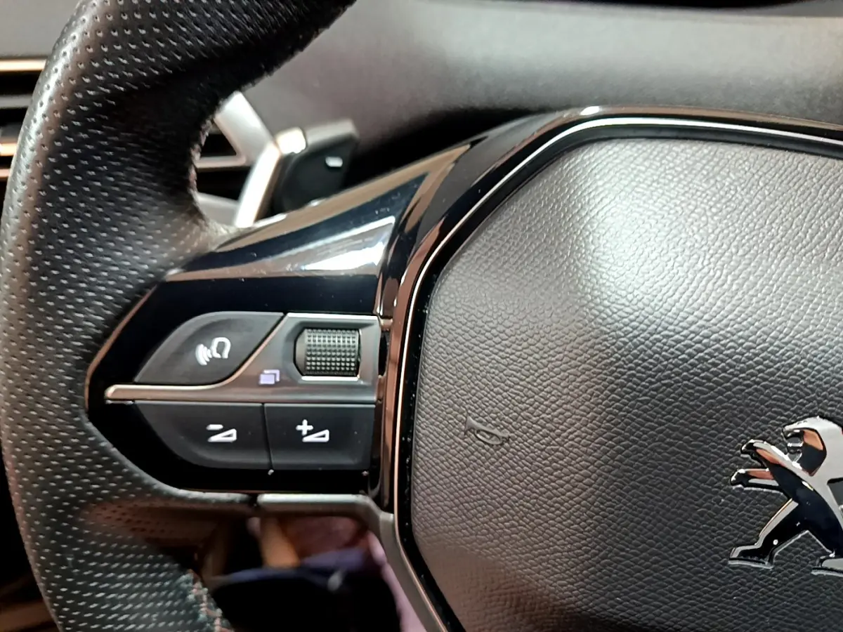 Gros plan sur le volant cuir noir du Peugeot 3008 2023, avec commandes multifonctions et logo lion chromé au centre.