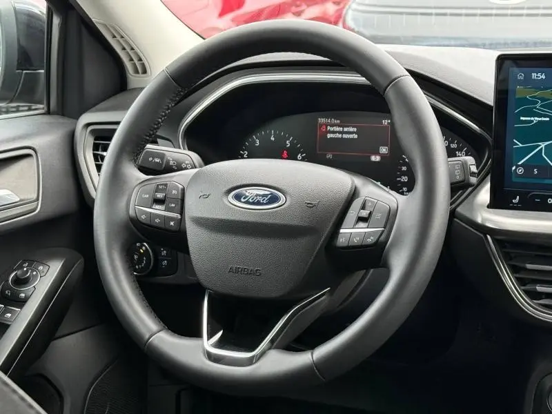 Vue rapprochée du volant noir de la Ford Focus SW 2023 avec commandes intégrées et tableau de bord numérique.