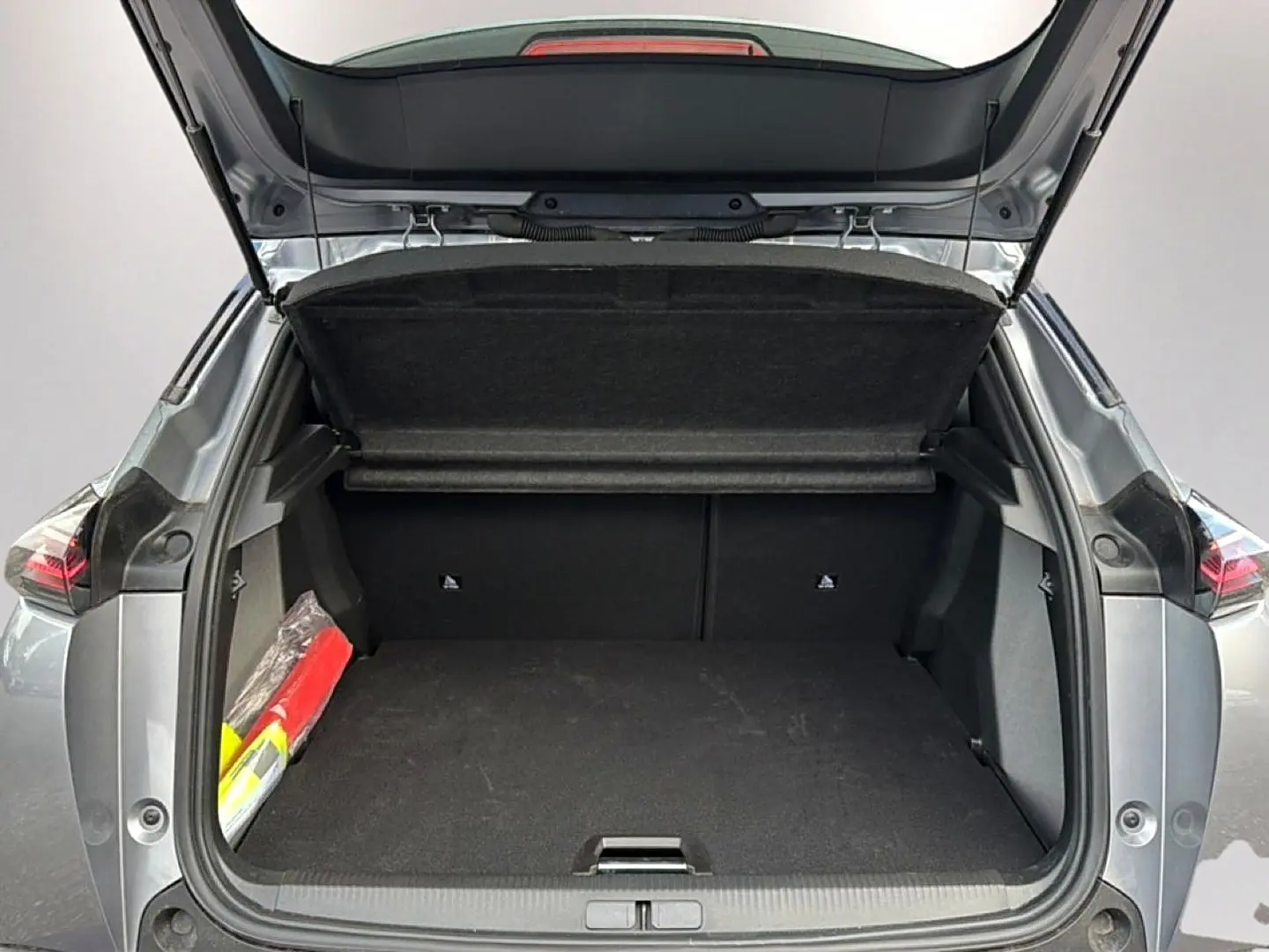 Coffre ouvert vu de l'arrière d'un Peugeot 2008 gris artense avec cache-bagages relevé et triangle de sécurité visible.