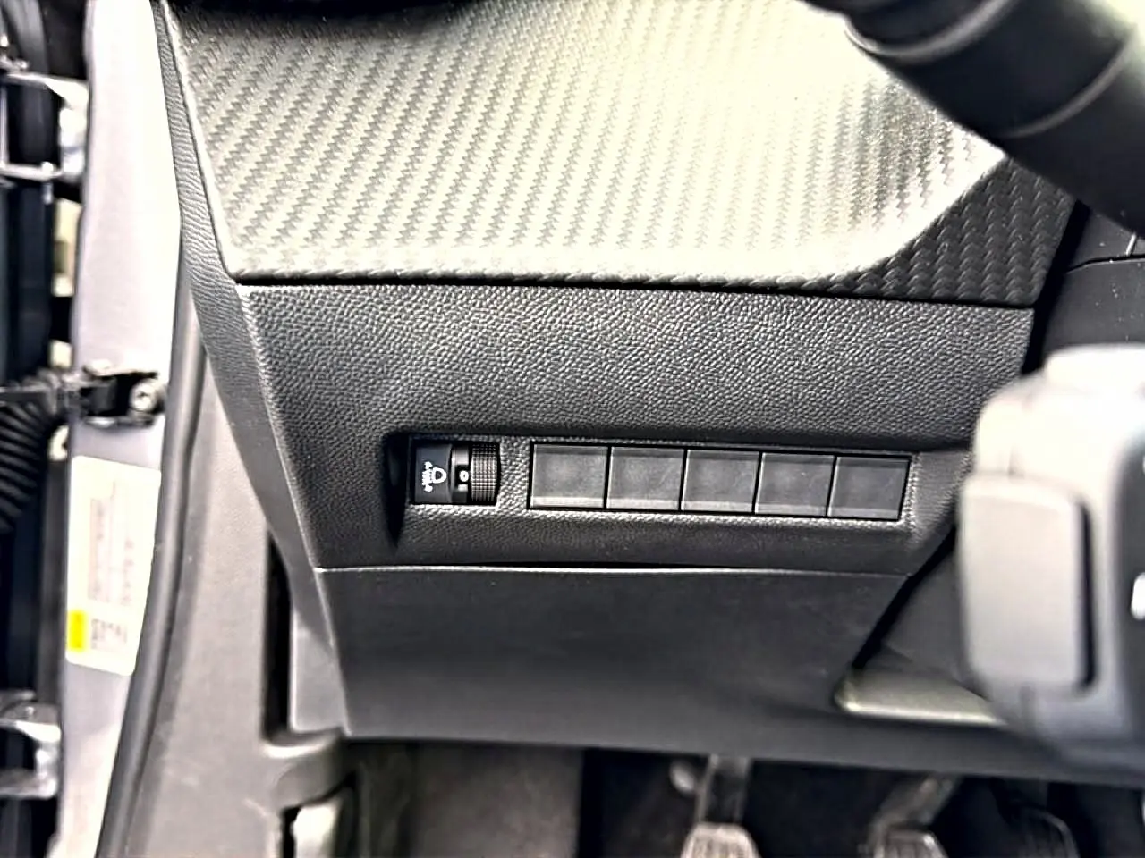 Détail intérieur côté gauche du tableau de bord noir avec commande de réglage des phares sur Peugeot 2008 gris Artense.
