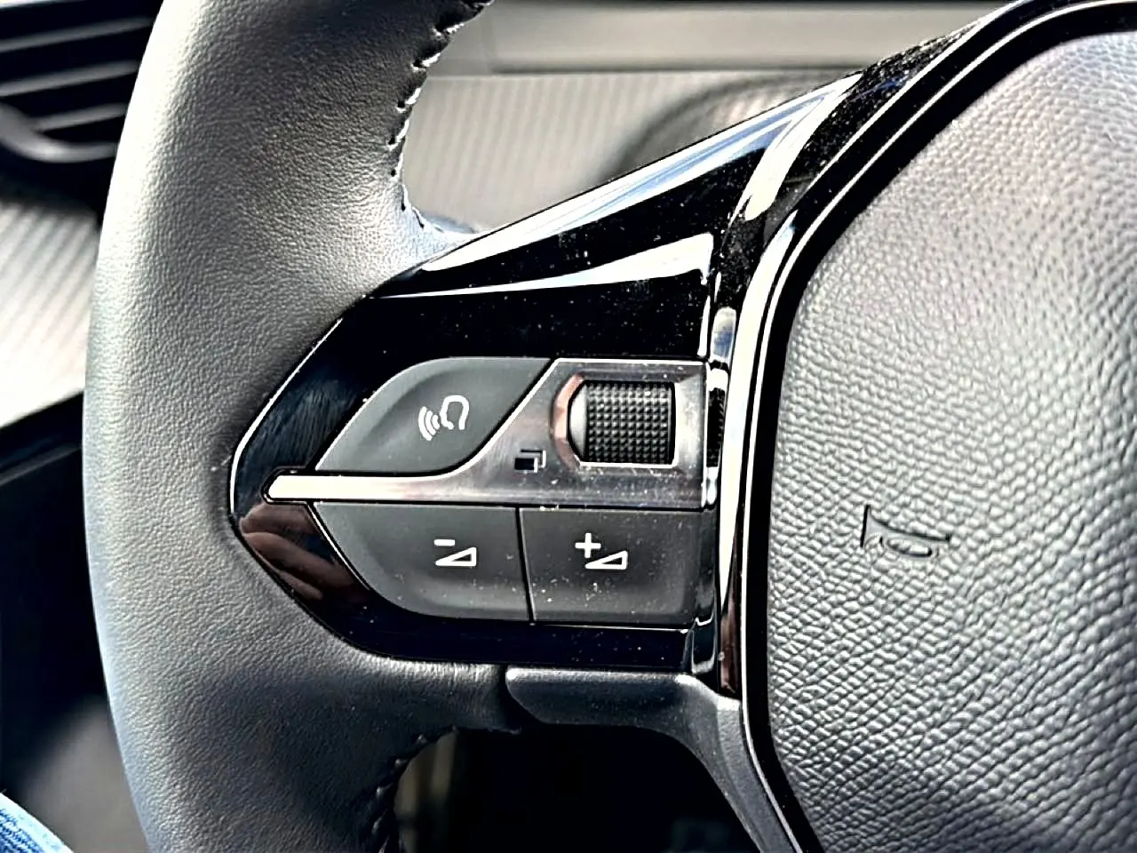 Gros plan sur les commandes gauche du volant en cuir noir du Peugeot 2008 gris Artense, avec boutons de volume et appel mains libres.